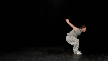 Açık gri elbiseli genç adam siyah arka planda hip-hop yapıyor..