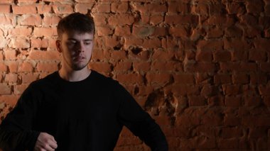 Siyah elbiseli genç adam kırmızı tuğla duvara karşı hip hop dansı yapıyor..