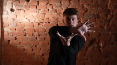 Siyah elbiseli genç adam kırmızı tuğla duvara karşı hip hop dansı yapıyor..
