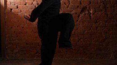Siyah elbiseli genç adam kırmızı tuğla duvara karşı hip hop dansı yapıyor..