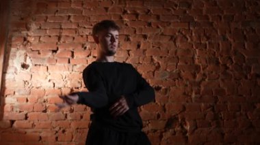 Siyah elbiseli genç adam kırmızı tuğla duvara karşı hip hop dansı yapıyor..