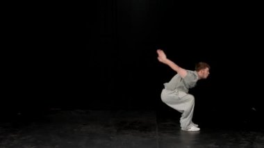 Açık gri elbiseli genç adam siyah arka planda hip-hop yapıyor..