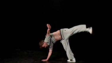 Açık gri elbiseli genç adam siyah arka planda hip-hop yapıyor..