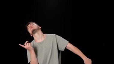 Açık gri elbiseli genç adam siyah arka planda hip-hop yapıyor..