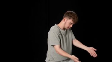 Açık gri elbiseli genç adam siyah arka planda hip-hop yapıyor..