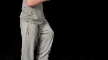 Açık gri elbiseli genç adam siyah arka planda hip-hop yapıyor..