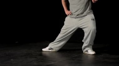Açık gri elbiseli genç adam siyah arka planda hip-hop yapıyor..