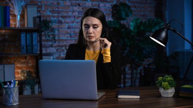 Ofiste çalışan bir iş adamı. Genç iş kadını masa başında geç saatlere kadar çalışıyor, dizüstü bilgisayar kullanıyor, kulaklık takıyor, müşteriyle konuşuyor, klavyede yazıyor, belgelere bakıyor..