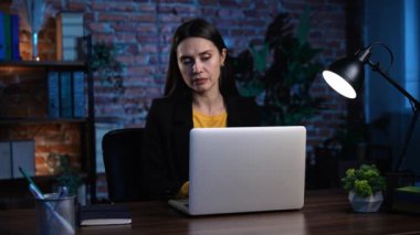 Ofiste çalışan bir iş adamı. Genç iş kadını geç saatlere kadar ofis dairesinde çalışıyor, dizüstü bilgisayar kullanıyor, klavyeye mesaj yazıyor, cevapları düşünüyor, fikir üretiyor ve e-posta gönderiyor..