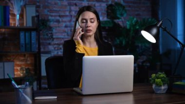 Ofiste çalışan bir iş adamı. Genç iş kadını geç saatlere kadar ofis dairesinde çalışıyor, dizüstü bilgisayar kullanıyor, telefonlara cevap veriyor ve telefonda konuşuyor, ciddi bir ifade..