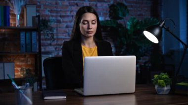 Ofiste çalışan bir iş adamı. Genç iş kadını ofiste geç saatlere kadar çalışıyor, dizüstü bilgisayar kullanıyor, e-posta yazıyor, cevapları düşünüyor, fikir üretiyor, mesaj yolluyor..