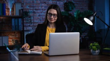 Ofiste çalışan bir iş adamı. Genç iş kadını geç saatlere kadar ofiste çalışıyor, dizüstü bilgisayar kullanıyor, iş arkadaşıyla görüntülü konuşma yapıyor, deftere yazıyor..