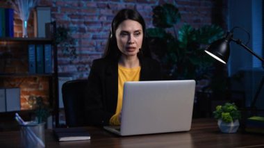 Ofiste çalışan bir iş adamı. Genç iş kadını masa başında geç saatlere kadar çalışıyor, dizüstü bilgisayar kullanıyor, kulaklık takıyor, müşteriyle konuşuyor, klavyede yazıyor, belgelere bakıyor..