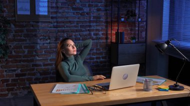 Günlük rutin yaşam tarzı konsepti. Ofisteki genç esmer kadın gece geç saatlere kadar çalışıyor, iş kadını masada oturuyor, bilgisayarını kullanıyor, pozitif yüz ifadesi düşünüyor..