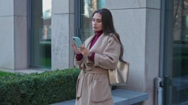 Günlük rutin yaşam tarzı konsepti. Sabahları genç esmer bir kadın işe gitmek için sabah yürüyüşünden zevk alıyor. Sokakta durmuş gülümsüyor, akıllı telefondan mesaj atıyor..