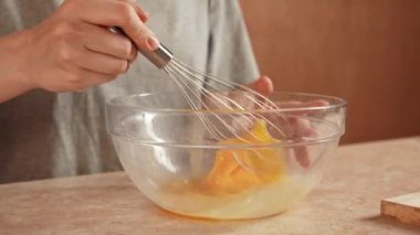 Günlük ev yemeği rutini. Evdeki masada oturan kadın waffle kahvaltısı için hamur hazırlıyor cam kasede yumurta çırpıyor. Yavaş çekim.