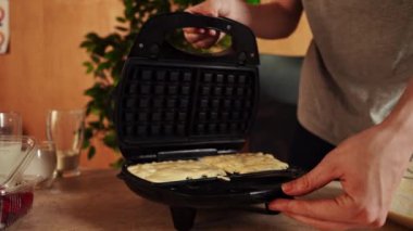 Günlük ev yemeği rutini. Evdeki masada oturan kadın waffle kahvaltısı için hamur hazırlıyor. Formlara hamur koyuyor ve waffle makinesini kapatıyor. Hazırlanmayı bekliyor..