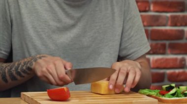 Günlük ev yemeği rutini. Adam öğle yemeği hazırlıyor. Evdeki masada oturan ve sandviçleri hazırlayan, tahtanın üzerinde bıçakla sert peynir kesen bir adam ekmeğin üzerine koyar..