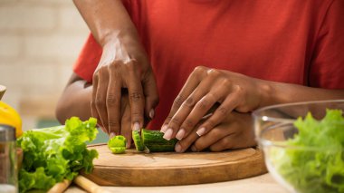 Mutlu aile mutfakta birlikte yemek pişiriyor. Afro-Amerikan anne ve küçük oğlu sağlıklı bir yemek hazırlıyor, annesinin oğlunun salatalığı bıçakla kesmesine yardım ederken yakın plan çekimleri yapıyor, oğlanların elini tutuyor..