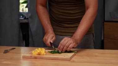 Günlük ev yemeği rutini. Adam yemek hazırlıyor. Yetişkin bir adam mutfakta masada duruyor ve spagetti hazırlıyor, İtalyan sosu için yeşil aromatik dereotu ve sert peynir kesiyor. Yavaş çekim.