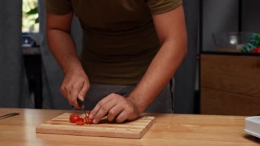 Günlük ev yemeği rutini. Adam yemek hazırlıyor. Yetişkin bir adam mutfakta masada duruyor ve İtalyan sosu için vişneli domates doğruyor. Yavaş çekim.