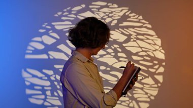 Renkli stüdyo geçmişi olan biri. Not defterinde yazan adamın portresi, spot ışıklarının altında dikiliyor. Mavi turuncu neon üzerinde izole edilmiş. Stüdyo arka planı var..