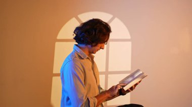 Renkli stüdyo geçmişi olan biri. Elinde kitap tutan, kitap okuyan, spot ışıklarında oturan, duvarında pencere desenleri olan bir adamın portresi..