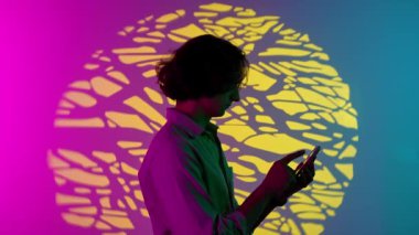 Renkli stüdyo geçmişinde telefonu olan biri. Akıllı telefondan süzülen sıradan giysili bir adamın portresi, Stüdyo arka planına sahip pembe mavi neon üzerinde gözlerden uzak duruyor..