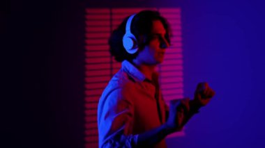 Renkli stüdyo geçmişinde telefonu olan biri. Kulaklıkla dans eden bir adamın portresi spot ışıklarıyla müzik dinliyor kırmızı mavi neon stüdyo arka planında güneşlik desenli..