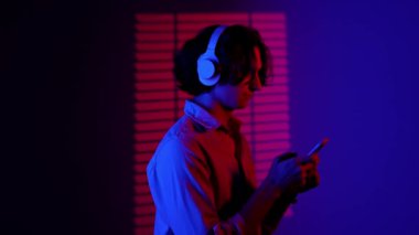 Renkli stüdyo geçmişinde telefonu olan biri. Kulaklıkla müzik dinleyen bir erkek siluetinin portresi. Sahne ışıkları altında kırmızı mavi neon arka planda kalıp ile izole edilmiş..