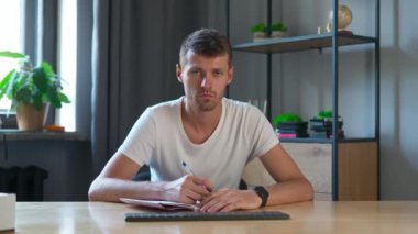 Çevrimiçi kursa katılan kişi. Erkek üniversite öğrencisi evde ders çalışıyor, masada oturuyor, internette ders dinliyor, not defterine başını sallıyor. Modern online eğitim.