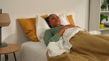 Günlük rutin yaşam tarzı konsepti. Genç Afro-Amerikalı kadın sabah yatak odasında pijamayla uyuyor, kadın uyanıyor, uzanıyor ve gülümsüyor..