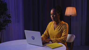 Günlük rutin yaşam tarzı konsepti. Akşamları geç saatlere kadar çalışan, dizüstü bilgisayar kullanan, klavyede yazan genç Afrikalı Amerikalı kadın.,
