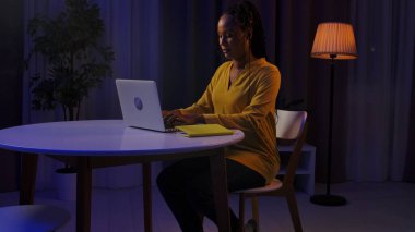 Günlük rutin yaşam tarzı konsepti. Akşamları geç saatlere kadar çalışan, dizüstü bilgisayar kullanan, klavyede yazan genç Afrikalı Amerikalı kadın.,