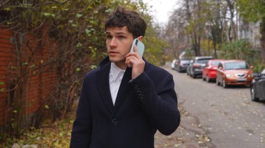 Günlük rutin yaşam tarzı konsepti. Sabahları genç işadamı şehirdeki ofisine günlük yürüyüşünün tadını çıkarıyor. Evrak çantasıyla sokakta yürüyor ve akıllı telefondan konuşuyor..