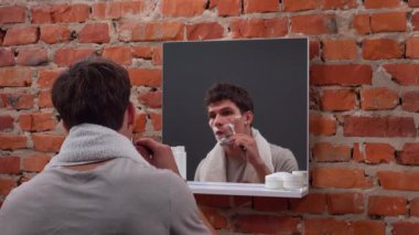 Günlük rutin yaşam tarzı konsepti. Sabah genç bir adam aynanın karşısında duruyor banyoda boynunda havluyla, günlük hijyen rutini yapıyor jiletle tıraş oluyor..