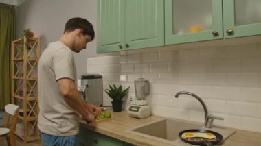 Günlük rutin yaşam tarzı konsepti. Genç adam sabah mutfakta sağlıklı bir kahvaltı hazırlıyor, taze meyve püresi yapıyor, kivi kesiyor ve blender koyuyor..