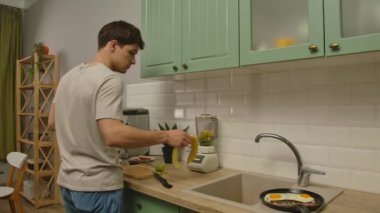 Günlük rutin yaşam tarzı konsepti. Genç adam sabahları mutfakta sağlıklı bir kahvaltı hazırlıyor, taze meyve suyu hazırlıyor, muz soyuyor ve blender ekliyor..
