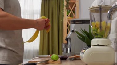 Günlük rutin yaşam tarzı konsepti. Genç adam sabahları mutfakta sağlıklı bir kahvaltı hazırlıyor, taze meyve suyu hazırlıyor, muz soyuyor ve blender ekliyor..