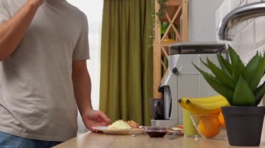 Günlük rutin yaşam tarzı konsepti. Sabahları mutfakta sağlıklı bir kahvaltı hazırlayan, yemek hazırlayan ve akıllı telefondan konuşan, elinde yemekle bekleyen genç bir adam..