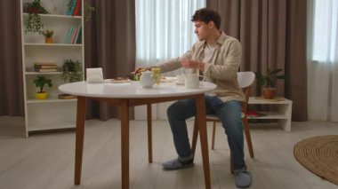 Günlük rutin yaşam tarzı konsepti. Sabahları genç bir adam mutfakta yemek odasında sağlıklı kahvaltının tadını çıkarıyor, masaya oturuyor kahve içiyor ve deftere yazıyor, plan günü ve liste hazırlıyor..