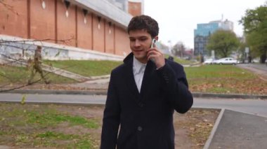 Günlük rutin yaşam tarzı konsepti. Sabahları genç işadamı şehirdeki ofisine günlük yürüyüşünün tadını çıkarıyor. Evrak çantasıyla sokakta yürüyor ve akıllı telefondan konuşuyor..