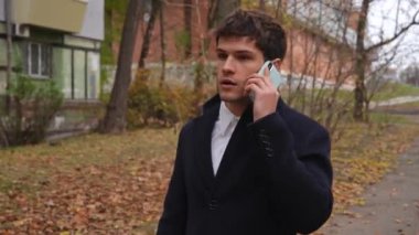 Günlük rutin yaşam tarzı konsepti. Sabahları genç işadamı şehirdeki ofisine günlük yürüyüşünün tadını çıkarıyor. Evrak çantasıyla sokakta yürüyor ve akıllı telefondan konuşuyor..