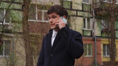 Günlük rutin yaşam tarzı konsepti. Sabahları genç işadamı şehirdeki ofisine günlük yürüyüşünün keyfini çıkarıyor. Elinde evrak çantasıyla caddede duruyor ve akıllı telefonuyla konuşuyor..