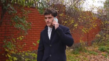 Günlük rutin yaşam tarzı konsepti. Sabahları genç işadamı şehirdeki ofisine günlük yürüyüşünün tadını çıkarıyor. Evrak çantasıyla sokakta yürüyor ve akıllı telefondan konuşuyor..