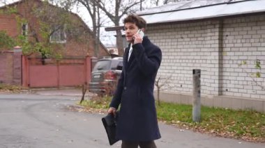 Günlük rutin yaşam tarzı konsepti. Sabahları genç işadamı şehirdeki ofisine günlük yürüyüşünün tadını çıkarıyor. Evrak çantasıyla sokakta yürüyor ve akıllı telefondan konuşuyor..