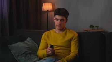 Günlük rutin yaşam tarzı konsepti. Akşamları işten sonra evde dinlenen, oturma odasında kanepede oturup televizyon izleyen, oyun oynayan, video oyunu oynayan genç adam, pozitif ifade..
