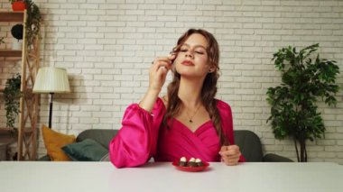 Tatlılar ve tatlılar reklam konsepti. Genç bir kadın masada oturuyor ve çikolata yiyor, ısırıyor ve çiğniyor, tatlı tatlı atıştırmanın tadını çıkarıyor, mutlu bir ifade..