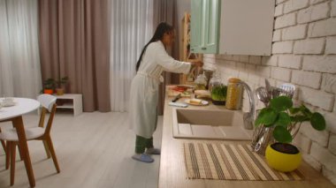Günlük rutin yaşam tarzı konsepti. Sabahları mutfakta sağlıklı bir kahvaltı hazırlayan Afro-Amerikalı genç bir kadın kızarmış ekmek hazırlıyor ve ekmeğe bıçakla yumuşak peynir sürüyor..