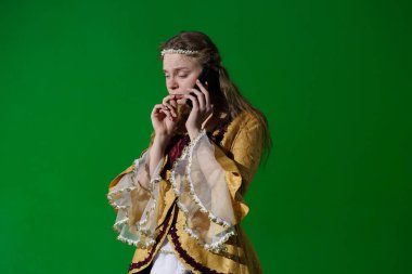 Tarihsel reklam konsepti. Krom anahtar yeşil ekran arka planda antik kıyafetli bir kadın. Rönesans elbisesi içinde, akıllı telefondan konuşan şüpheci yüzlü bir kadın..